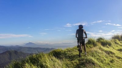 A cyclist on a mountain ridge enjoys a sunny day with a stunning view.