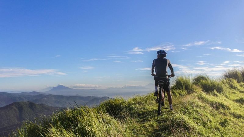 A cyclist on a mountain ridge enjoys a sunny day with a stunning view.